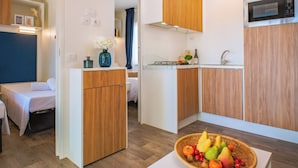 Een compacte keuken met houten kastjes, een magnetron en een kleine eethoek met een tafel en stoelen.