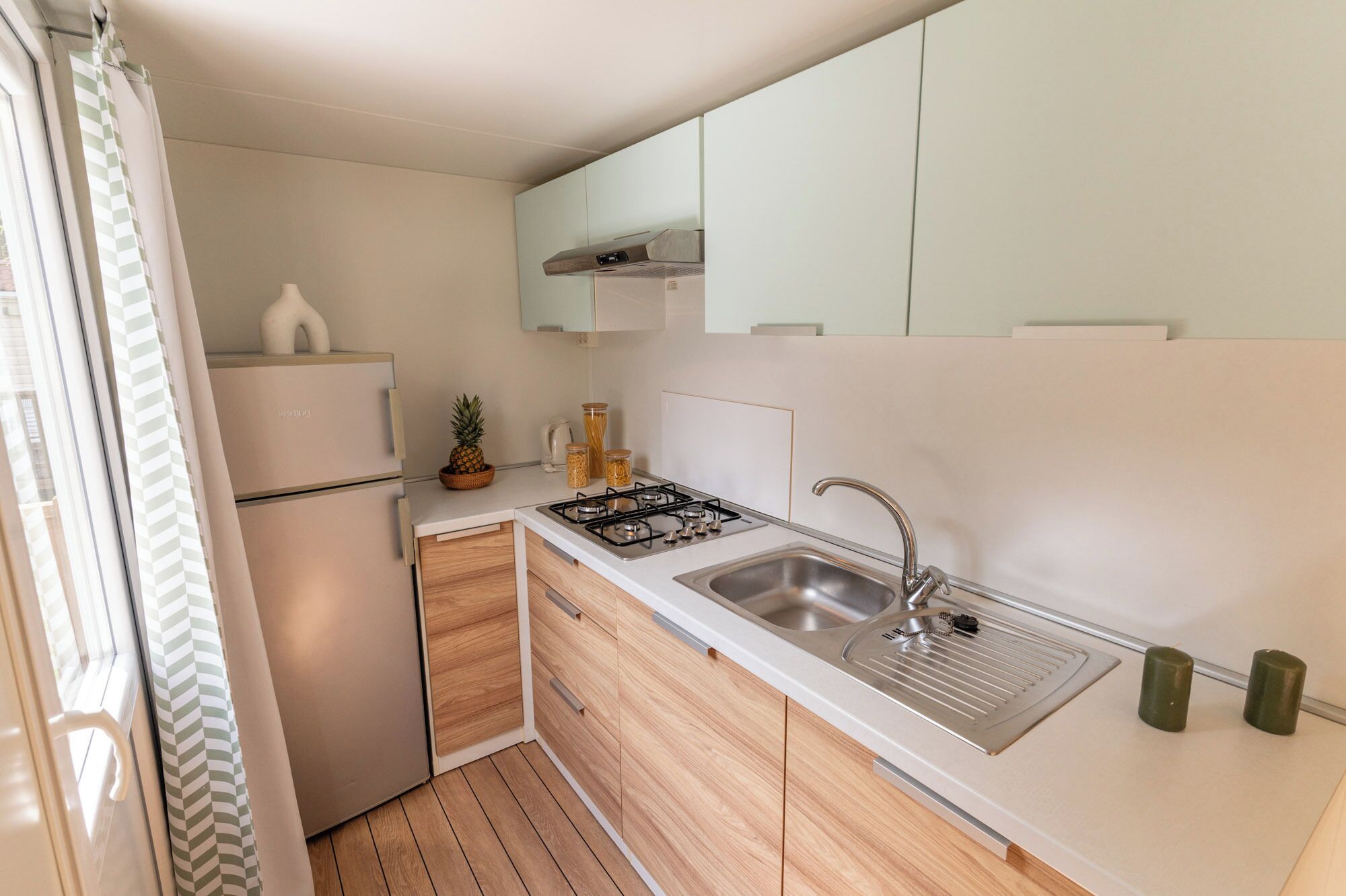 A compact kitchen with a built-in gas stove, a stainless steel sink, and wooden cabinets.