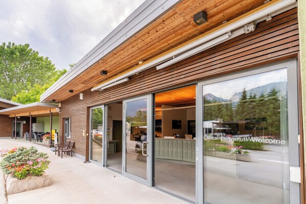 A modern building with wooden slats on the exterior, large glass doors, and a view of mountains through the windows. - Club del Sole Due Laghi Levico (Levico Terme)