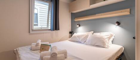 A hotel room with a bed, towels, a nightstand, a window with curtains, and built-in shelves.
