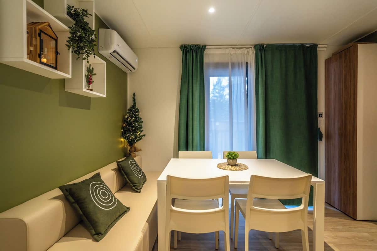 Een eethoek met een witte tafel en stoelen, een kleine kerstboom en een groen gordijn.