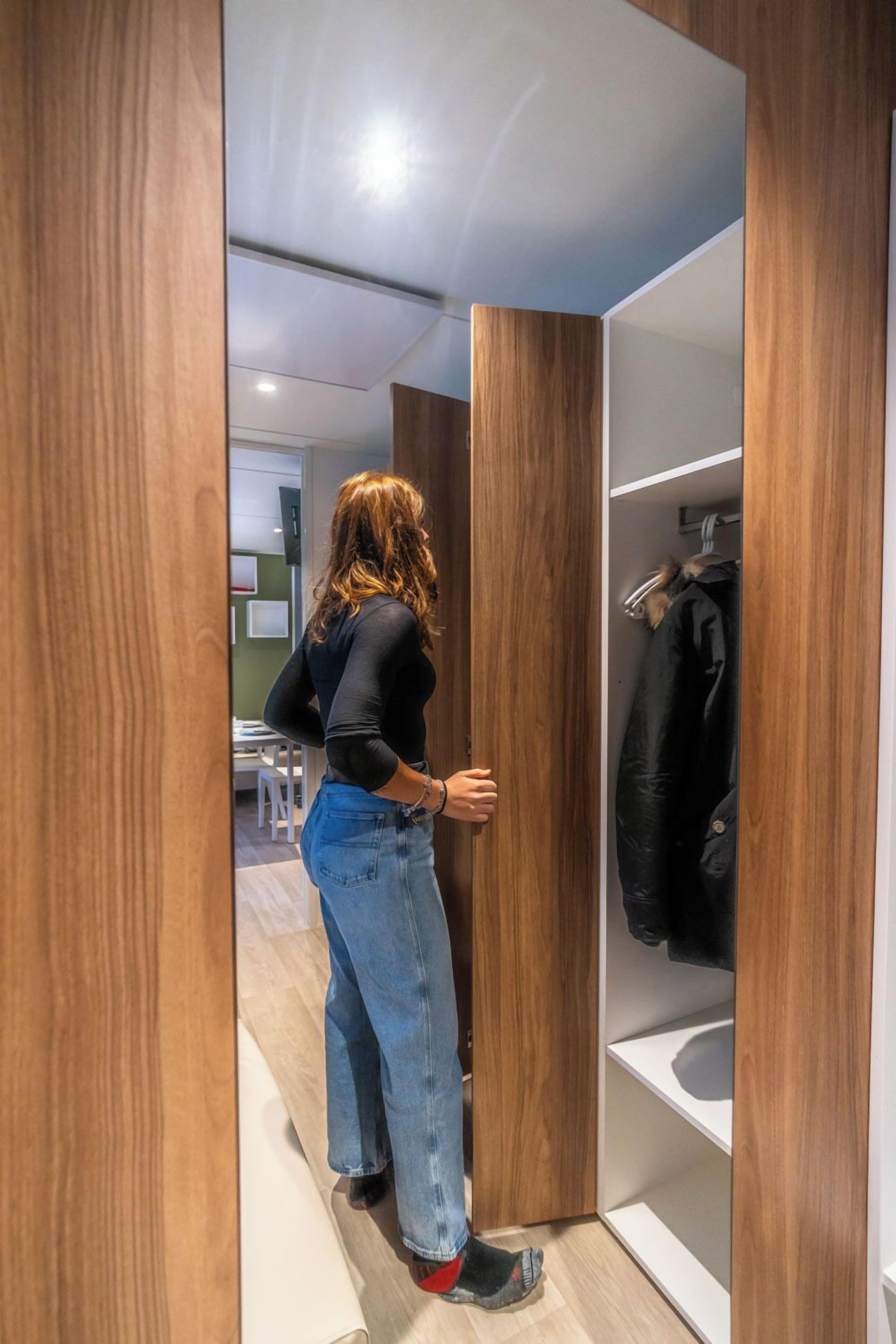 A person in a modern room with wooden paneling, a white sink, and a coat rack.