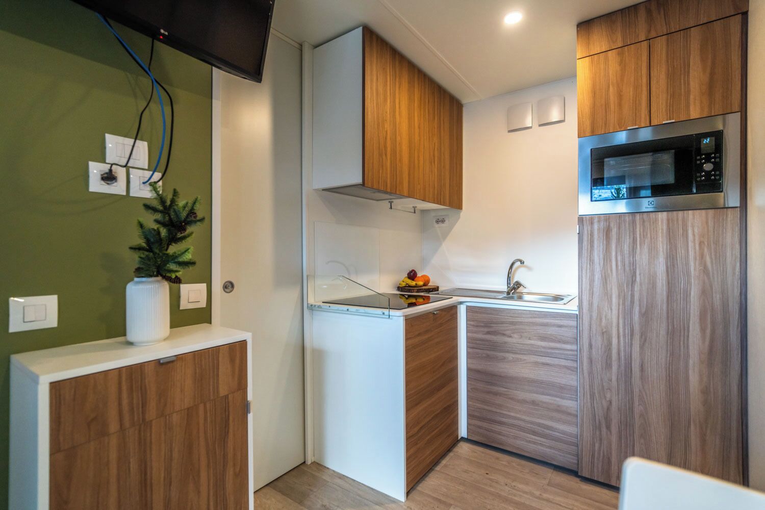 Een kleine keuken met een magnetron, spoelbak en houten kastjes.