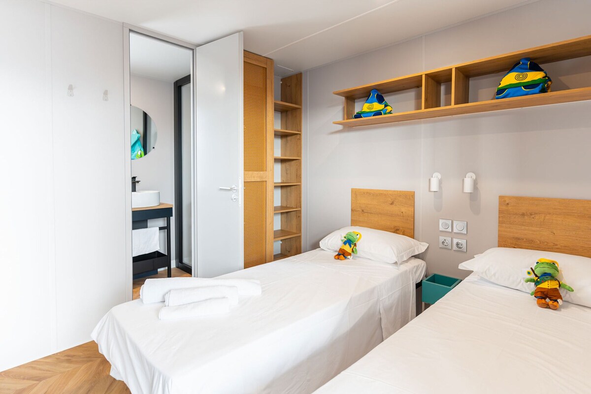 Hotelkamer met twee bedden, een houten hoofdbord, een plank met speelgoed, een spiegel en een badkamer met wastafel en toilet.