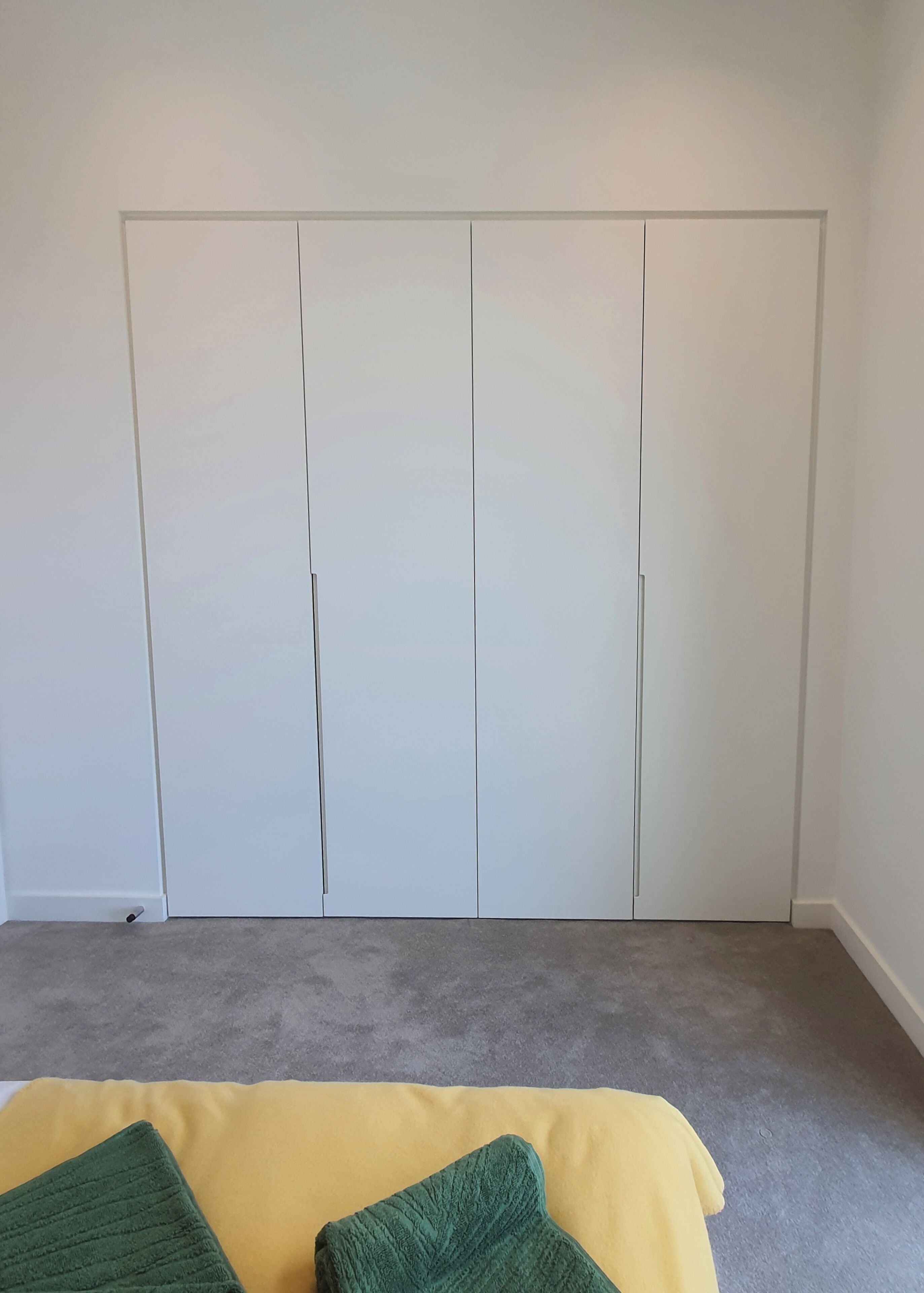 Une pièce avec un tapis gris, un lit jaune et une armoire blanche.