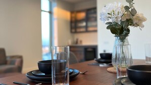 A dining table set with black plates, clear glasses, and a vase with white flowers.