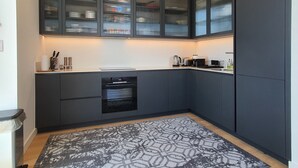 A modern kitchen with dark cabinetry, a built-in oven, and a patterned rug.