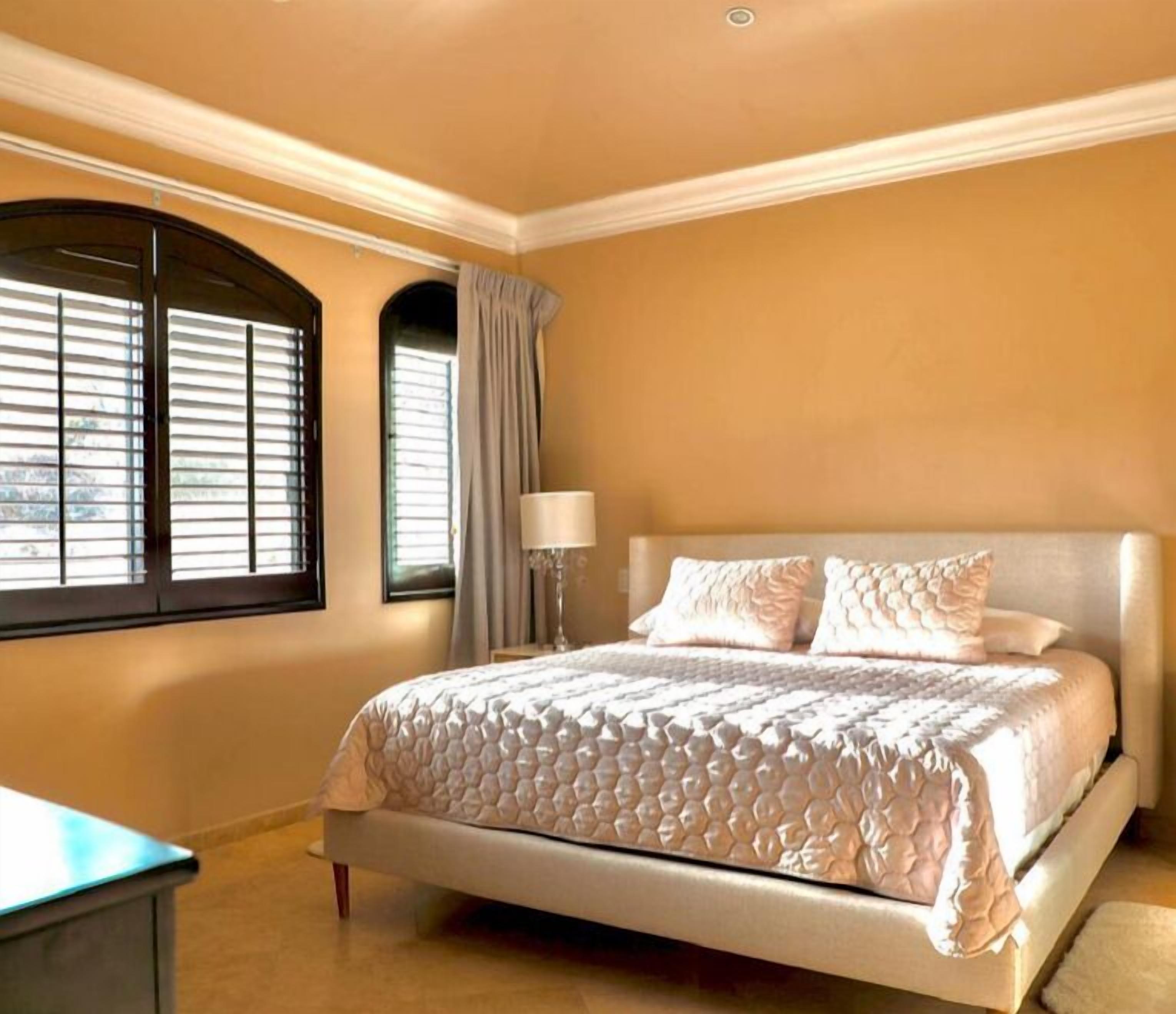 Un dormitorio con una cama grande, una mesita de noche, una lámpara y una ventana con persianas.