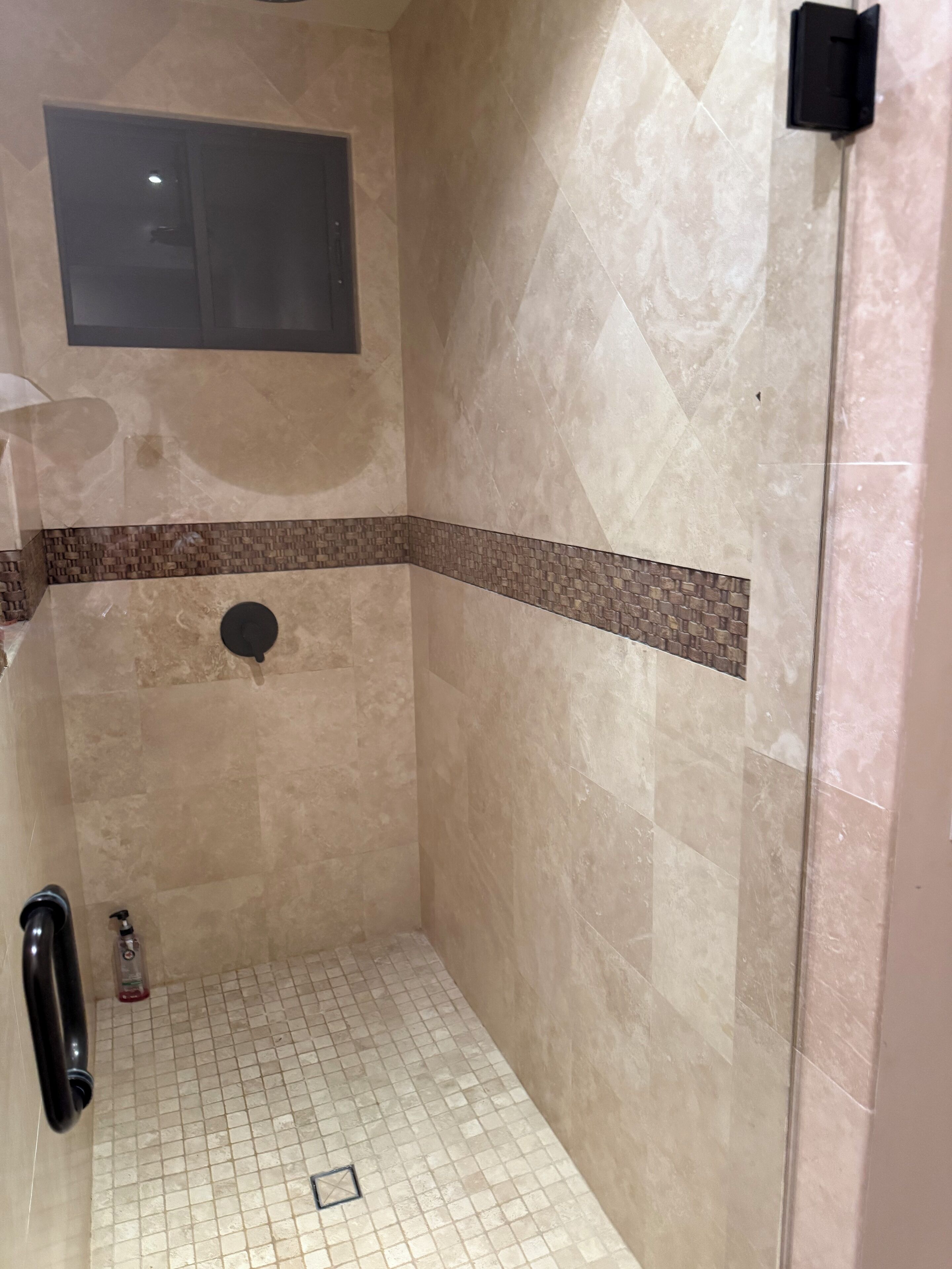 A small, tiled shower area with a window above and a handrail on the left.