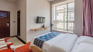 A hotel room with a bed, a TV mounted on the wall, a window with a view of buildings, and a door with a sign. - Kunming Panju Hotel (Kunming)