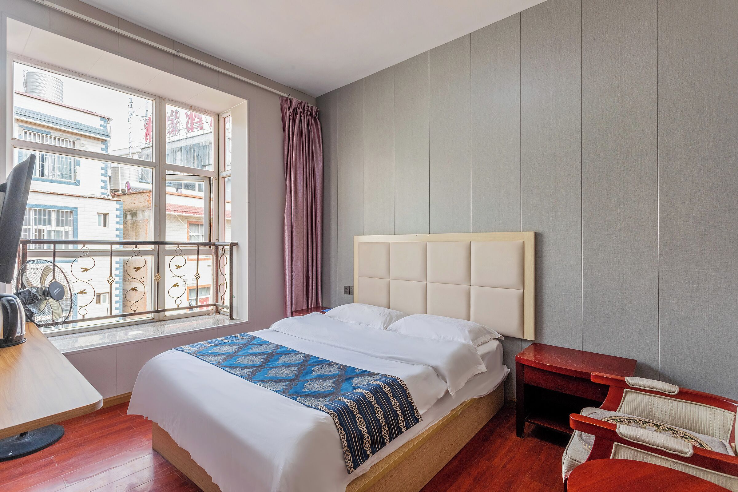 Une chambre d’hôtel avec un lit, un bureau, une chaise, une fenêtre donnant sur des immeubles et un rideau.