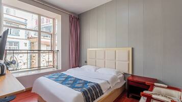 Une chambre d’hôtel avec un lit, un bureau, une chaise, une fenêtre donnant sur des immeubles et un rideau.