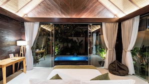 Camera da letto moderna con porta in vetro che dà su una zona piscina, soffitto in legno e vista su piante tropicali.