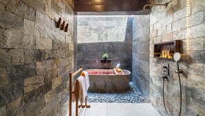 Un bagno con pareti in pietra, una vasca freestanding, una doccia e un piccolo ripiano con articoli da toilette.