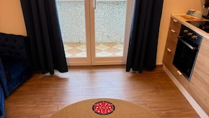 Una habitación con un tapete redondo marrón que presenta un diseño de montaña y una porción de pizza, un sofá negro, un mueble de madera con una estufa, y vistas a través de una puerta de cristal.