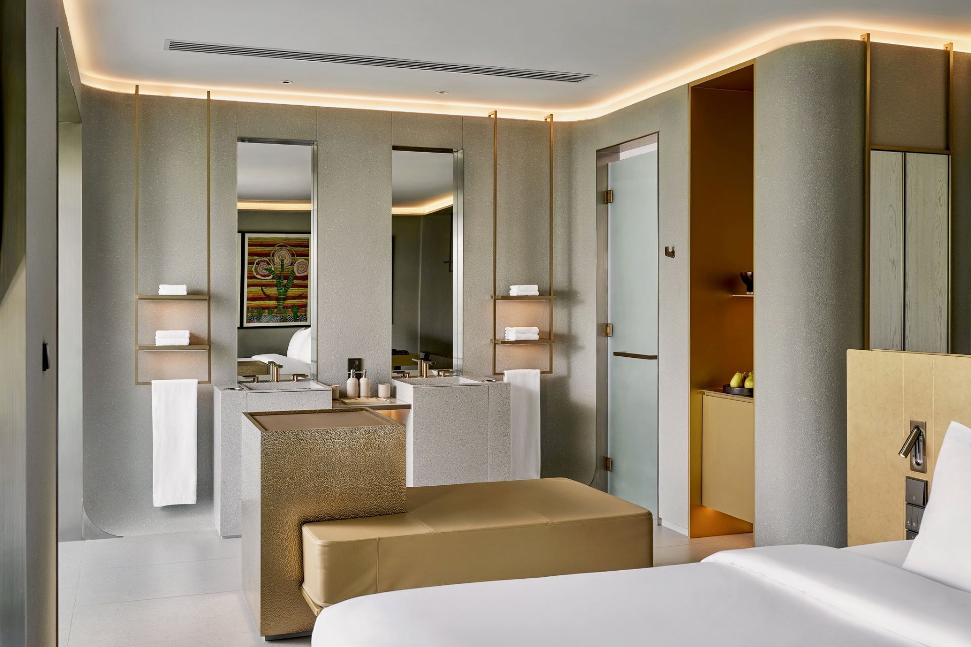 A modern hotel room with a large bed, a seating area, a vanity with a mirror, and a bathroom visible through an open door.