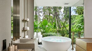A modern bathroom with a freestanding bathtub, a large mirror, and a view of lush greenery outside. - Villa Zai (Karon)