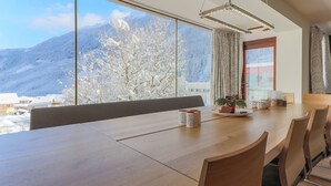 Een eetgedeelte met een grote tafel, stoelen en een uitzicht op besneeuwde bergen.