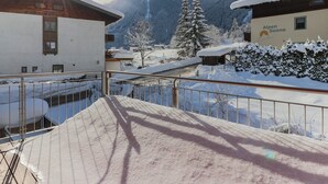 Een besneeuwd berglandschap met gebouwen, waaronder een hotel genaamd "Alpen Sonne", met een balkon en een metalen hekwerk.