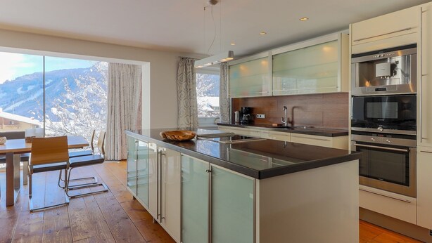 Een moderne keuken met een groot schiereiland, roestvrijstalen apparatuur en uitzicht op besneeuwde bergen.