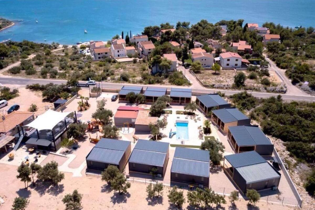 Une vue aérienne d’une station balnéaire comprenant plusieurs bâtiments, une piscine et offrant une vue dégagée sur la mer.