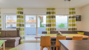 Moderni olohuone, jossa on sohva, ruokapöytä ja tuoleja. Siinä on liukuovet, jotka johtavat ulos parvekkeelle.
