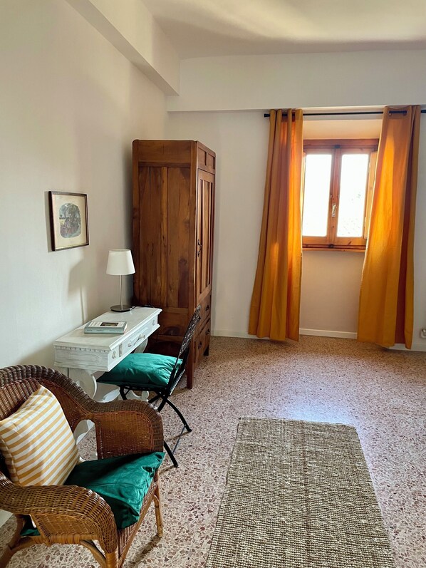A room with a wooden wardrobe, a white desk with a lamp, wicker chairs, a green cushion, and a patterned rug. - OLIVE TREES - SAN DONATO FARMHOUSE (Calenzano)