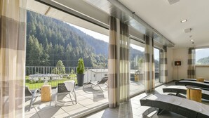 Une chambre d’hôtel moderne dotée d’un balcon, de grandes fenêtres et offrant une vue sur une montagne boisée.