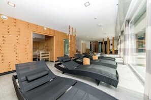 Un moderno espacio de spa con tumbonas negras, paredes de madera y entrada de vidrio.