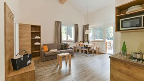 Un salon moderne avec un canapé, une table basse et un coin repas. On y trouve un meuble en bois avec des étagères et un four à micro-ondes posé sur le comptoir.