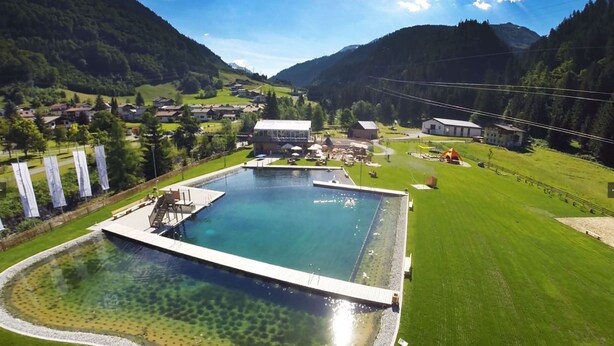 Une grande piscine avec une terrasse, entourée d’une pelouse bien entretenue et dominée par un paysage montagneux.