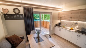 A modern kitchen with wooden cabinets, a dining area with a table and chairs, and a view of a wooden deck through a glass door. - Thermal Canopy Tree House With Riviera Tickets (Brežice)