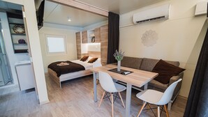A compact room with a bed, a dining table with chairs, a small kitchenette, and an air conditioning unit. - Thermal Canopy Tree House With Riviera Tickets (Brežice)