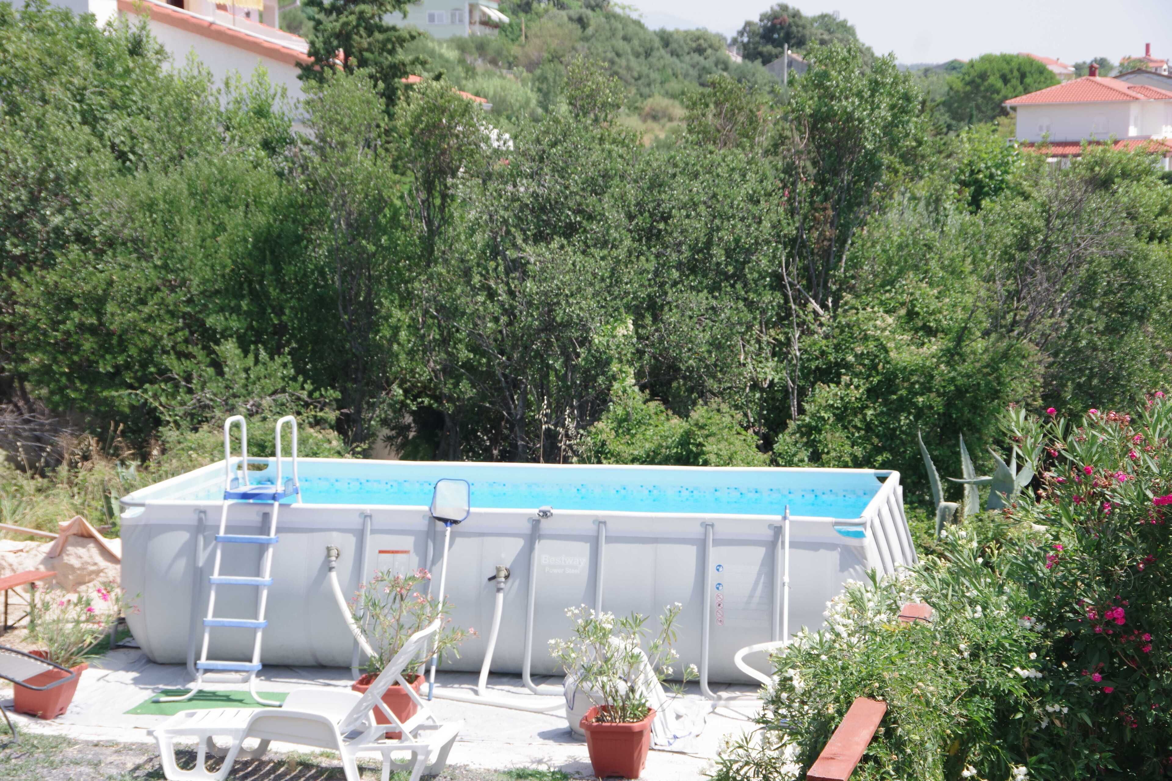 An outdoor swimming pool with a ladder, surrounded by potted plants and a white chair.