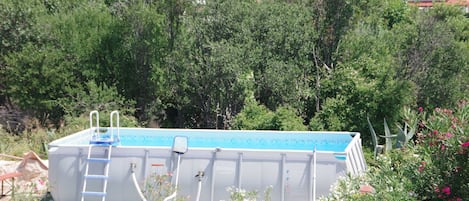 An outdoor swimming pool with a ladder, surrounded by potted plants and a white chair.