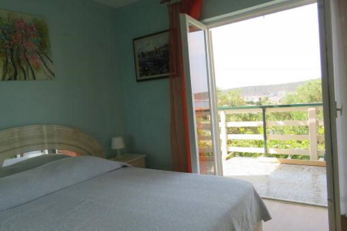A bedroom with a bed, a nightstand, a painting, and a view of a balcony with greenery.