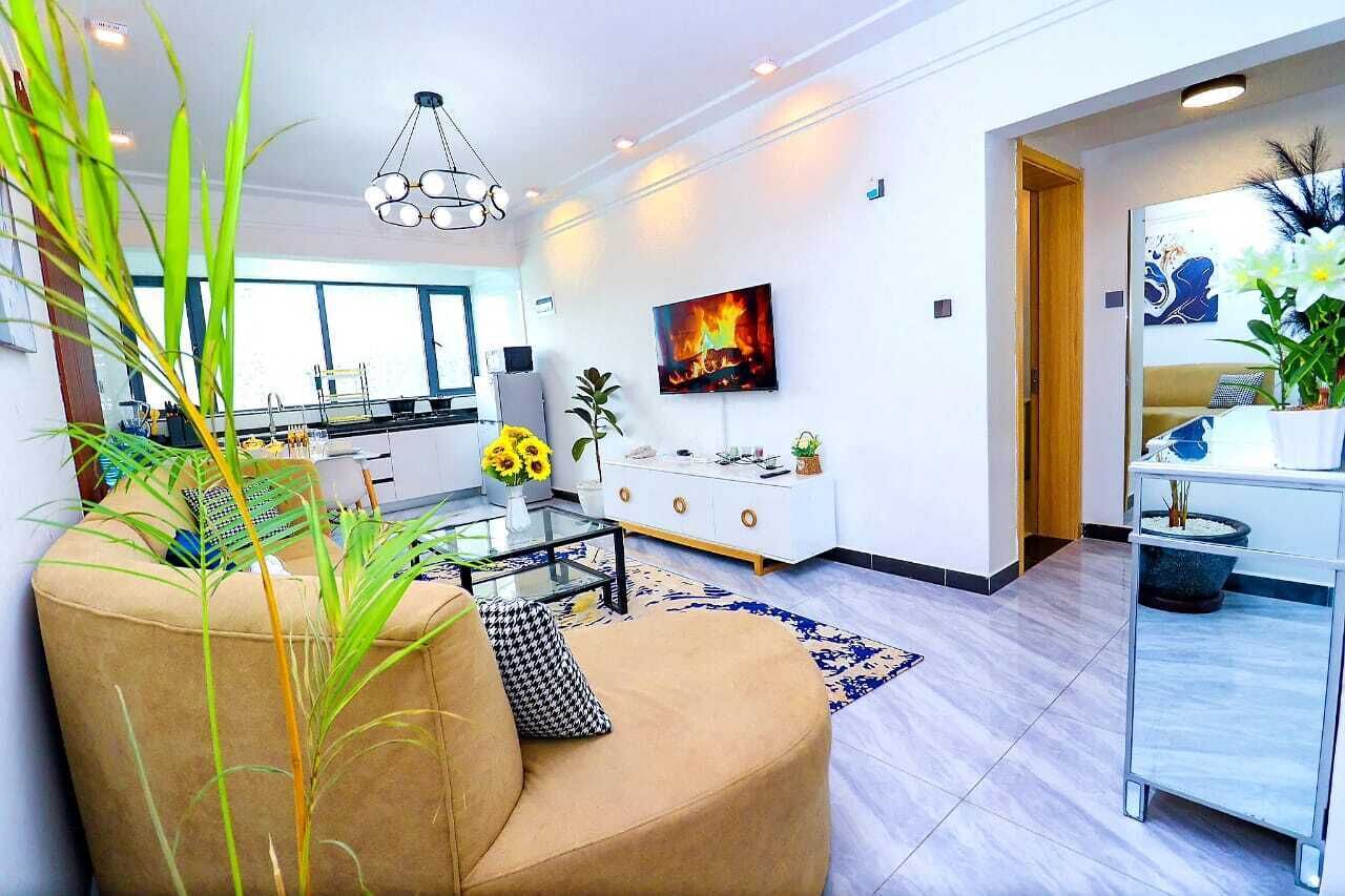 Uma sala de estar moderna com um sofá, uma mesa de centro de vidro e uma televisão fixada na parede.