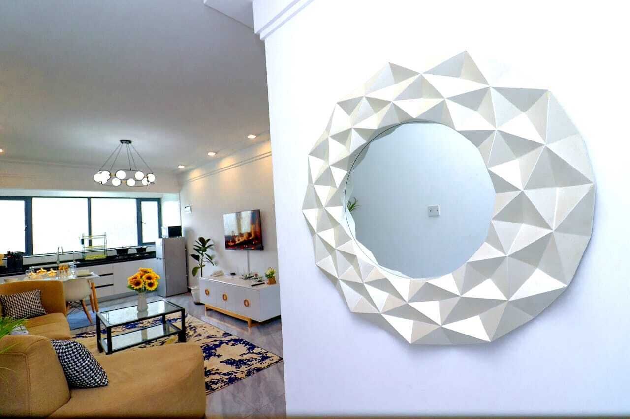 A modern living room with a geometric wall mirror, a sofa, a coffee table, and a TV.