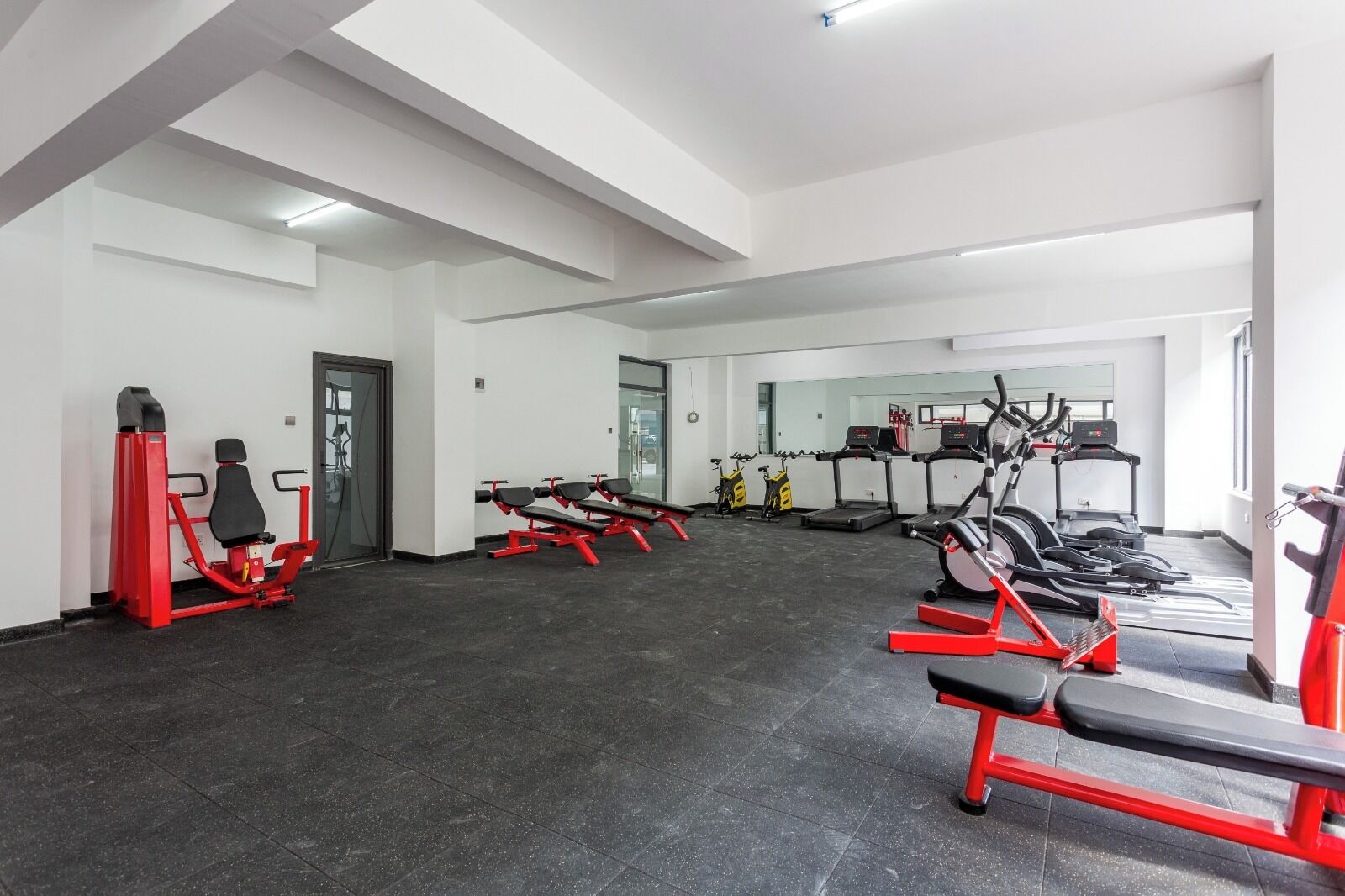 Une salle de sport équipée de machines de cardio, de postes d’entraînement avec poids et d’un mur recouvert de miroirs.