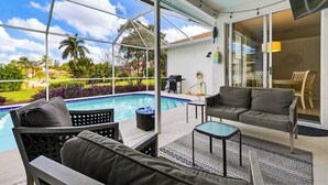 A covered outdoor area with a pool, seating, and a view of the landscape.