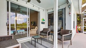 A covered outdoor area with a pool, wicker furniture, and a ceiling fan.