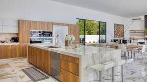 Une cuisine moderne avec des meubles en bois, un grand îlot central doté de tabourets de bar et une vue sur la verdure environnante.
