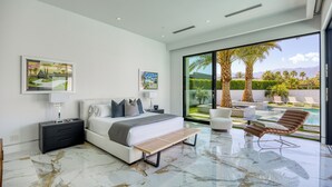 Une chambre moderne avec un grand lit, des tables de chevet, un banc et une vue sur une piscine et un espace extérieur.