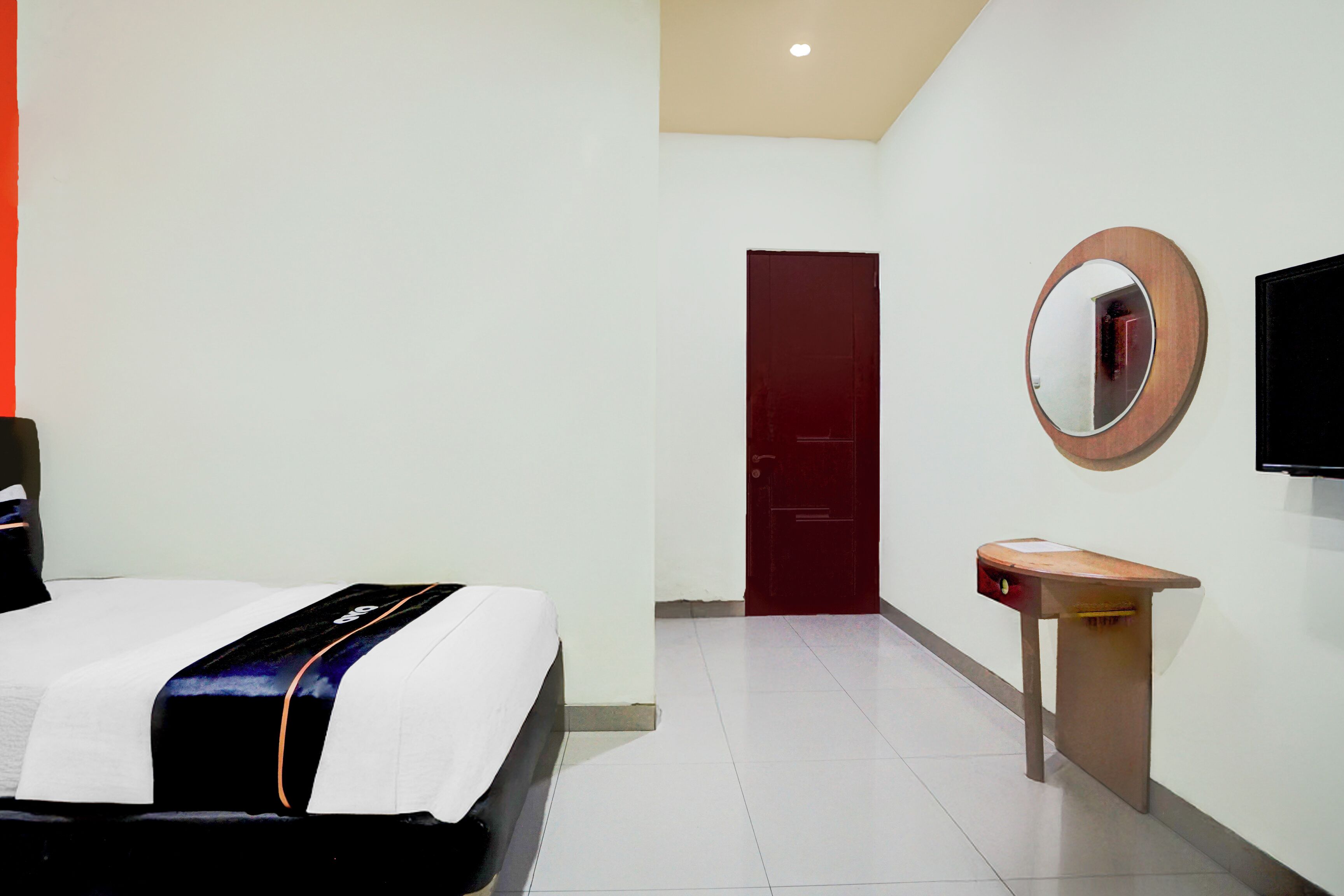 Una habitación de hotel con una cama, una mesita de madera con espejo, una puerta roja y un televisor de pantalla plana montado en la pared.