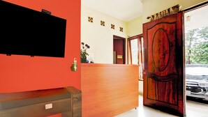 A reception area with a wooden desk, a flat-screen TV mounted on the wall, and a door leading outside. - Hotel O 76 Gayungsari (Surabaya)