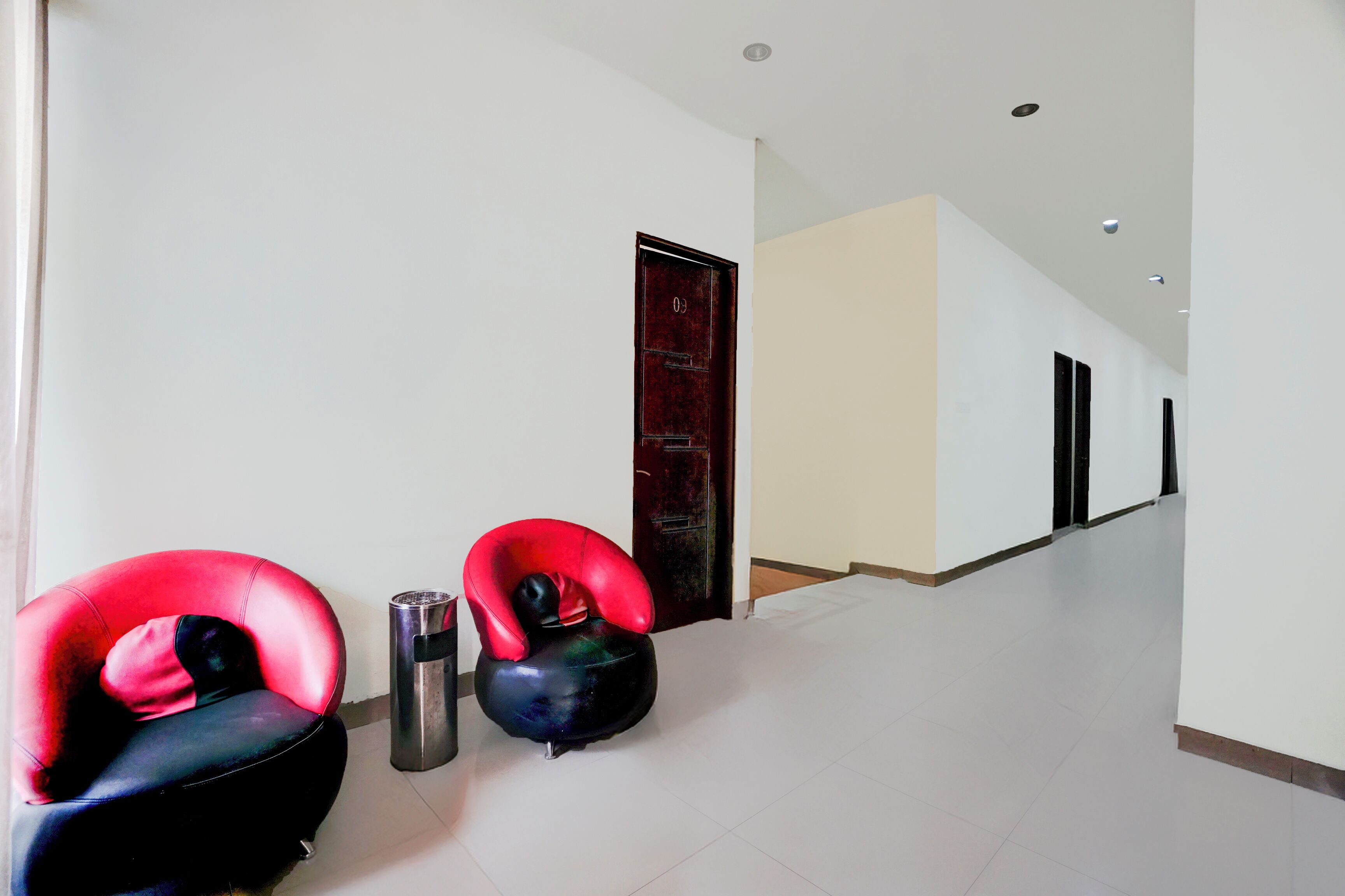 A hallway with two red chairs, a trash bin, and a door.