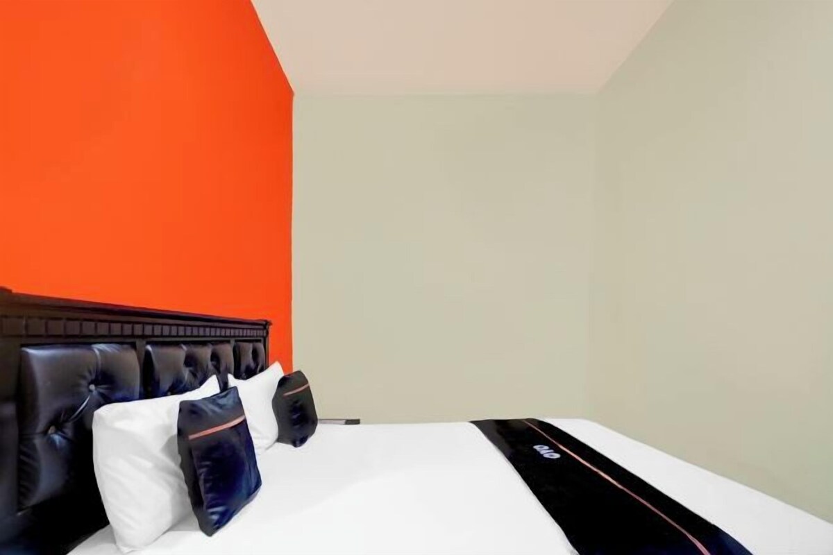 A hotel room with a bed, a headboard, and a plain wall.