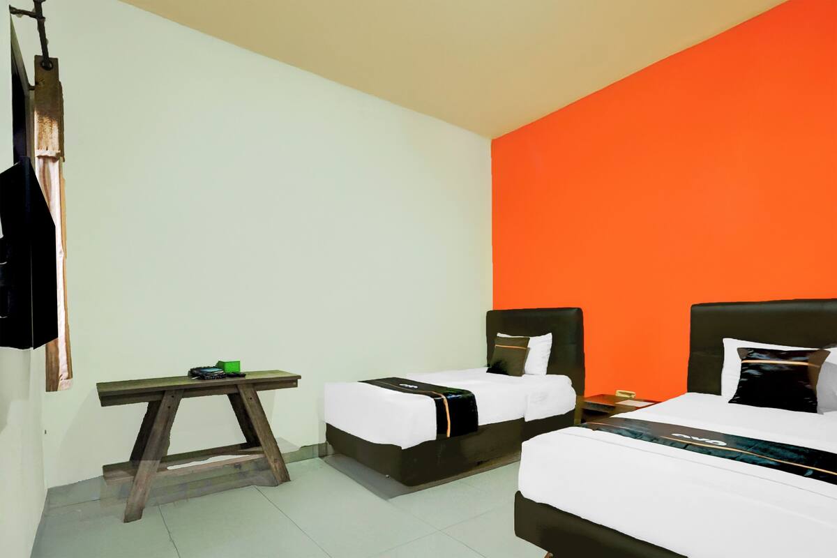 A hotel room with two beds, a wooden bench, and a TV mounted on the wall.