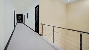 A long, narrow hallway with a tiled floor, a black door at the end, and a beige wall on the right side. - Hotel O 76 Gayungsari (Surabaya)