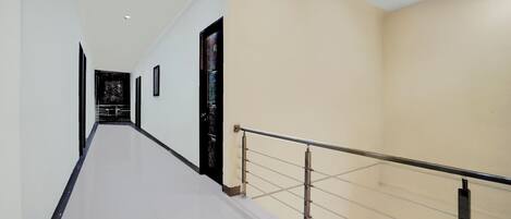 A long, narrow hallway with a tiled floor, a black door at the end, and a beige wall on the right side.